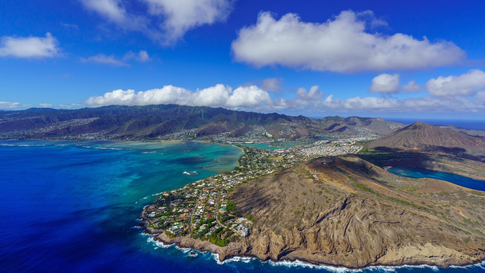 Wide aerial view across Oʻahu's coast, volcanic ridges, neighborhoods, and ocean