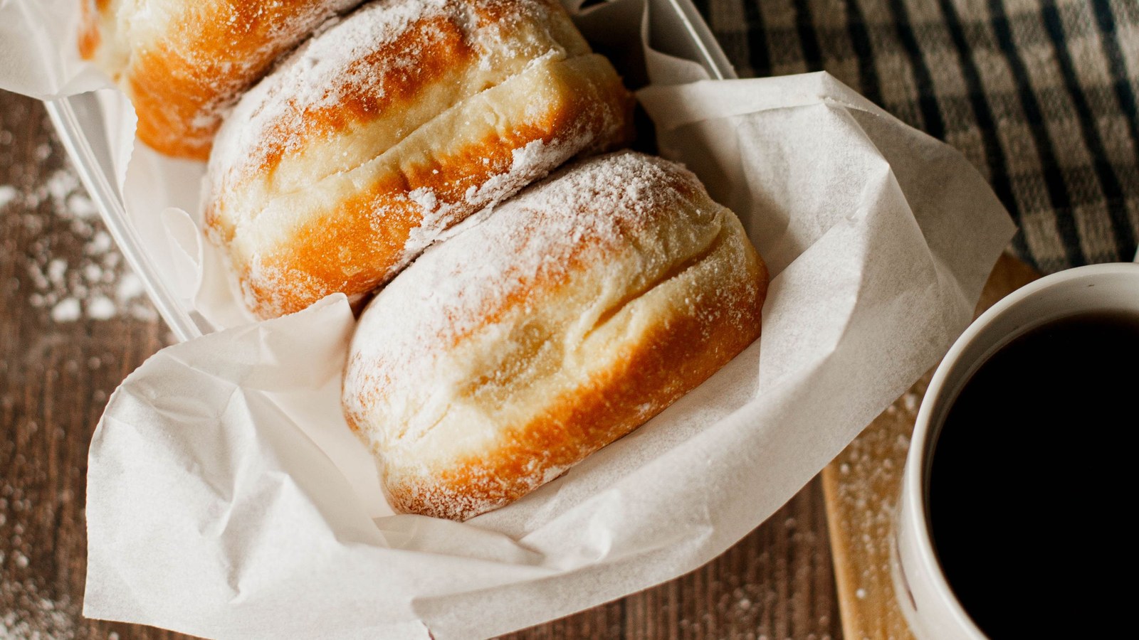 Illustrative stock photo of powdered donuts beside coffee.